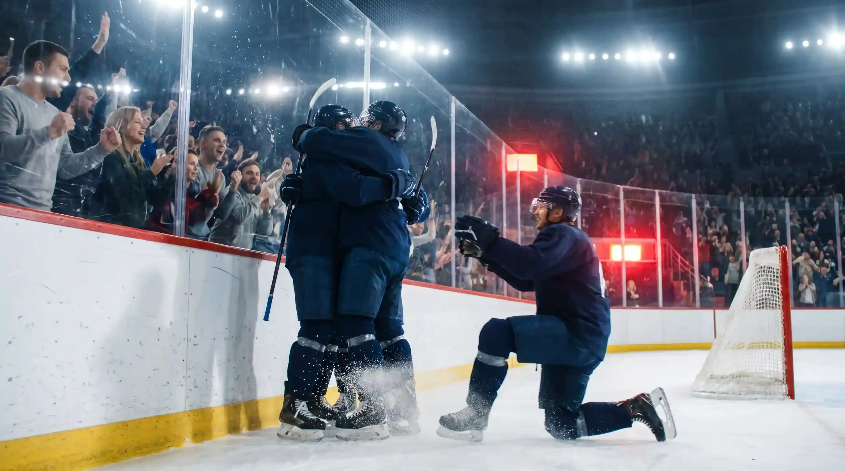 Hockey players celebrating a goal on ice with the red goal light illuminated behind the net