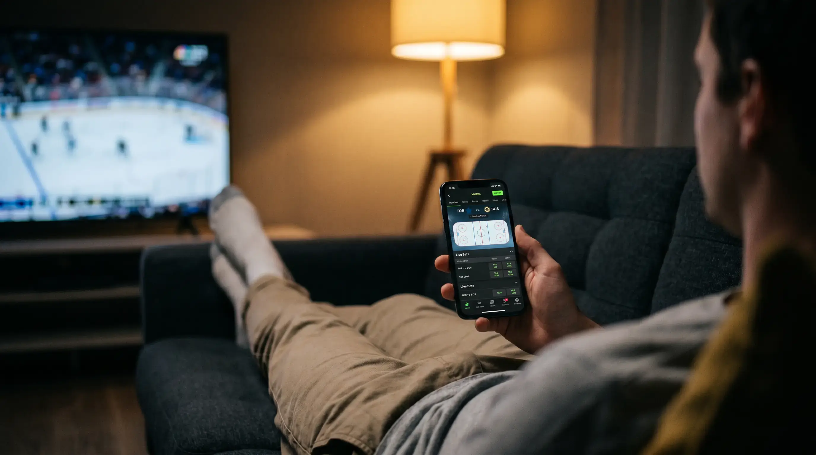Person holding a smartphone placing an NHL bet from a sofa in the evening